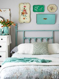 a white bed with blue headboard and pillows in a room filled with pictures on the wall