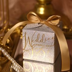 a small silver box with a gold ribbon tied around it on top of a table