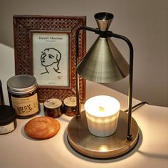 a lit candle sitting on top of a table next to jars and a framed picture