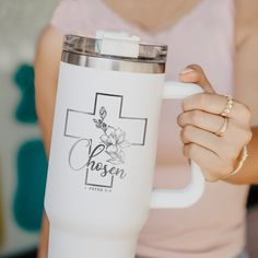 a woman holding a white coffee cup with a cross on it