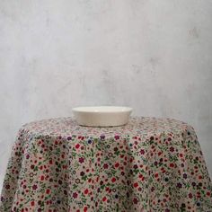 a white bowl sitting on top of a table covered in a flowered cloth next to a wall