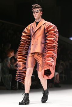 a man in an orange jacket and shorts on the runway