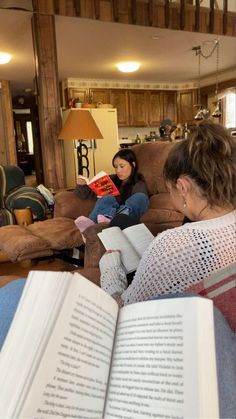 two women are sitting on a couch and reading books while another woman sits in the background