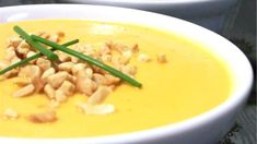 two white bowls filled with yellow soup and garnished with green onions on top