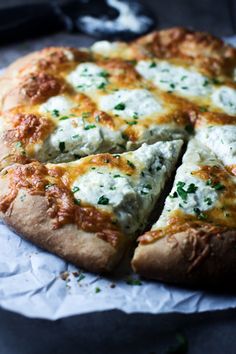 a pizza with cheese and parsley on it is cut into four pieces, sitting on wax paper