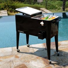 a cooler sitting on the side of a swimming pool next to a lawn and stone patio