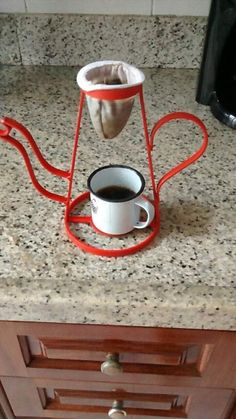 a cup of coffee sitting on top of a counter next to a red holder with a handle