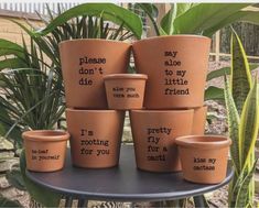 nine clay pots with sayings on them sitting on a table in front of some plants