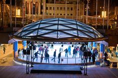 people skating on an ice rink at night in front of a large glass dome structure