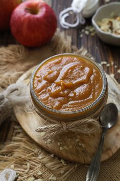 an apple pie in a glass jar on a wooden board with spoons next to it