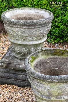 two cement planters sitting next to each other on top of gravel covered ground with bushes in the background