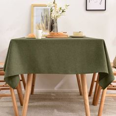 a table with two chairs and a green table cloth on it, in front of a white wall