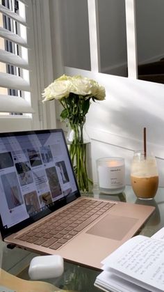 an open laptop computer sitting on top of a glass table next to a vase with flowers