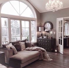 a living room filled with furniture and a chandelier hanging from the ceiling next to a large window