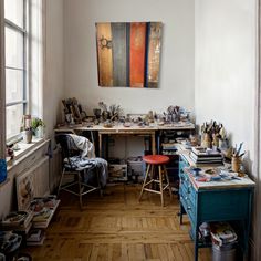 an artist's studio with various pieces of art on the desk and in the window