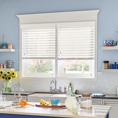 a kitchen with blue walls and white countertops has sunflowers on the window sill