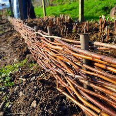 a fence made out of sticks in the middle of a field with people walking by