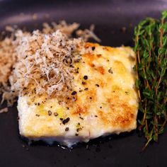 a piece of fish with parmesan sprinkles sits on a black plate