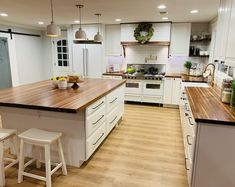 a large kitchen with white cabinets and wooden counter tops, along with two stools