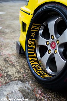 the front wheel of a yellow sports car with black spokes and red lettering on it