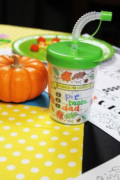 a green sippy cup sitting on top of a table next to an orange pumpkin