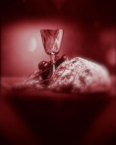 a wine glass sitting on top of a table next to some bread and grapes in front of a red background