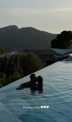 a man and woman kissing in an outdoor swimming pool with mountains in the back ground