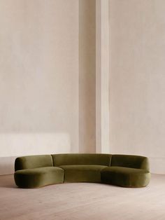 a green couch sitting on top of a hard wood floor next to a white wall