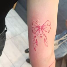 a woman's arm with a red bow tattoo on the left side of her arm