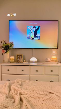 a flat screen tv mounted on the wall above a bed with white drawers and blankets