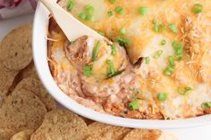 a white bowl filled with meat and cheese dip surrounded by tortilla chips on the side