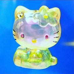 a glass hello kitty figurine sitting on top of a green object with pink and yellow eyes