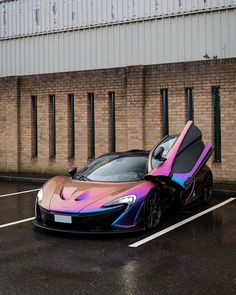 a pink and blue sports car parked in a parking lot next to a brick building