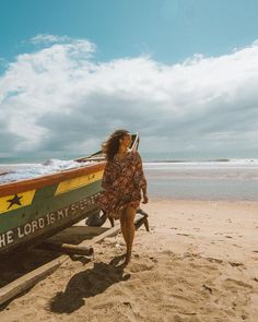 a woman walking on the beach next to a boat