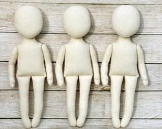 three white dolls standing next to each other on a wooden surface with wood planks behind them