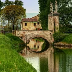 an old stone bridge over a river with statues on the top of it and green grass around