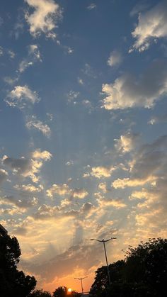 the sun is setting behind some clouds in the sky over trees and street lights on a city street