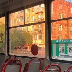 there are many empty seats on the bus in front of the window and buildings behind them