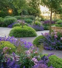 a garden filled with lots of purple and green flowers on top of a brick walkway