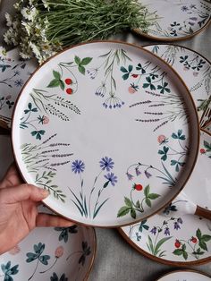 a person holding a plate with flowers on it next to other plates that have leaves and berries painted on them