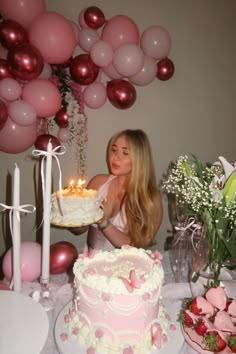 a woman sitting at a table with a cake in front of her and balloons behind her