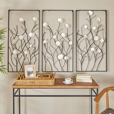 a wooden table topped with a coffee cup next to two metal wall art panels covered in white flowers