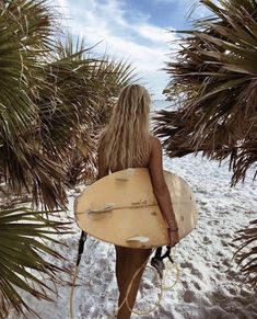 a woman holding a surfboard on top of a sandy beach next to palm trees