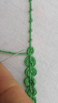 someone is stitching the end of a piece of green thread on a white surface