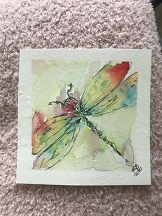 a watercolor drawing of a dragonfly sitting on top of a pile of carpet