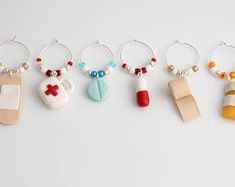 six different keychains with charms attached to them on a white surface, one has a red cross and the other is a bottle