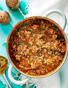 a pot filled with meat and vegetables on top of a blue cloth next to bread