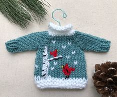 a knitted sweater ornament next to a pine cone