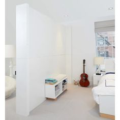 a bedroom with white walls and flooring has a guitar on the wall next to it