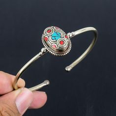 a person is holding a silver bracelet with red and blue beads